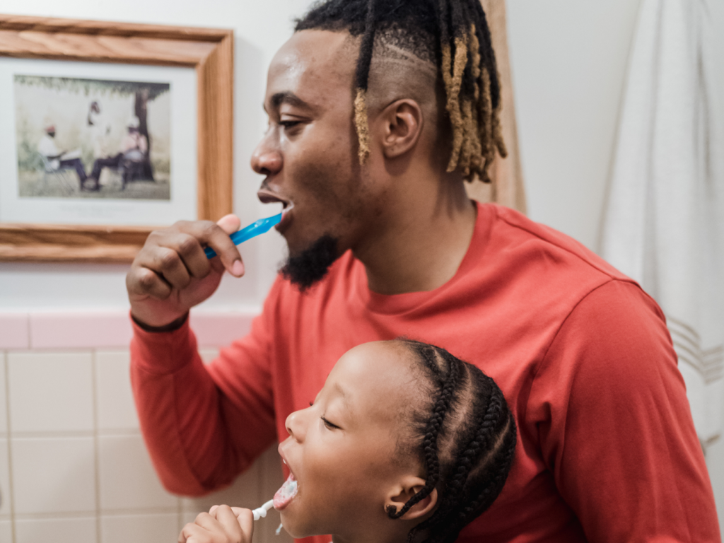 A child and adult brush their teeth together.